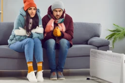No Heat at Home This Could Be the Reason Why - Man and woman freezing cold sitting near space heater, because their HVAC heating broke down Philadelphia